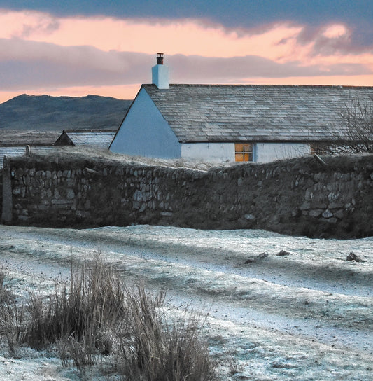 Cornish Christmas card showing frost on the ground in front of cottage with light in the window, Rough Tor in the background