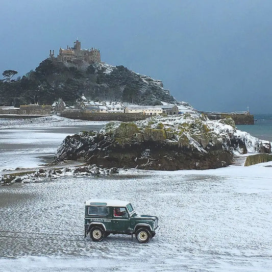 A snowy scene of a Landrover in front of St Michael's Mount