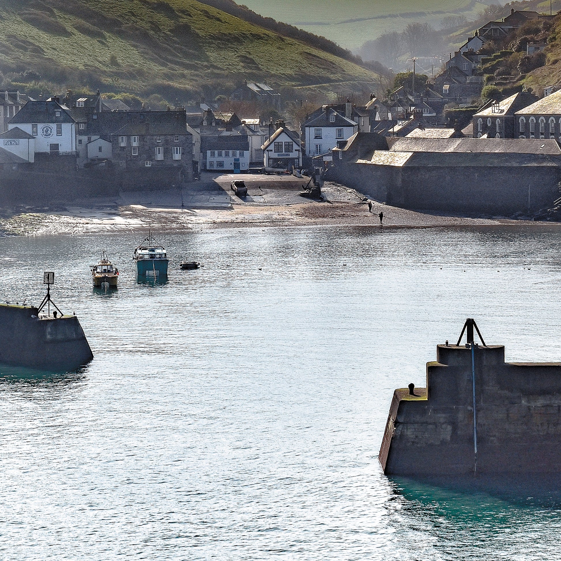 An Evocative Cornwall greetings card showing a quiet harbour scene at Port Isaac on Cornwall's north coast, looking through the harbour walls back towards the tiny village and valley beyond