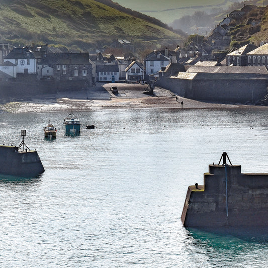 An Evocative Cornwall greetings card showing a quiet harbour scene at Port Isaac on Cornwall's north coast, looking through the harbour walls back towards the tiny village and valley beyond