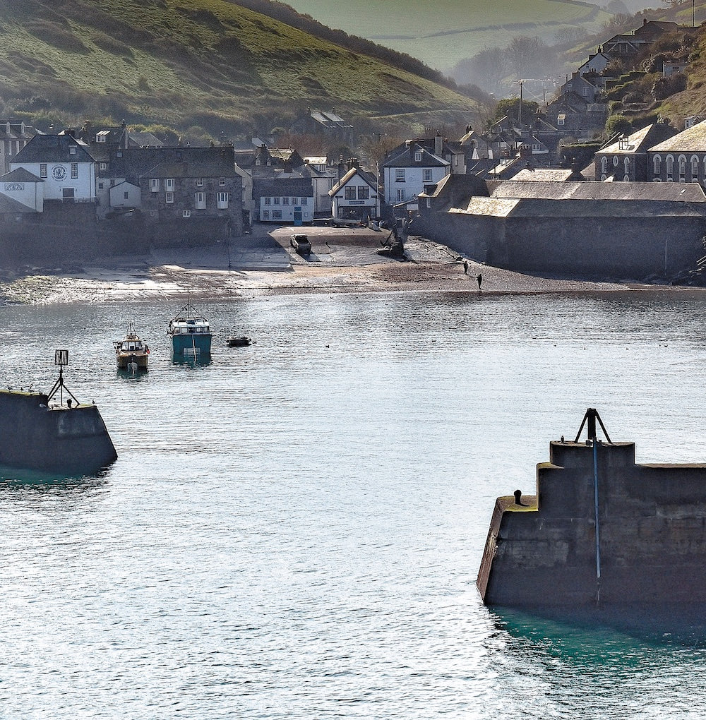 An Evocative Cornwall greetings card showing a quiet harbour scene at Port Isaac on Cornwall's north coast, looking through the harbour walls back towards the tiny village and valley beyond