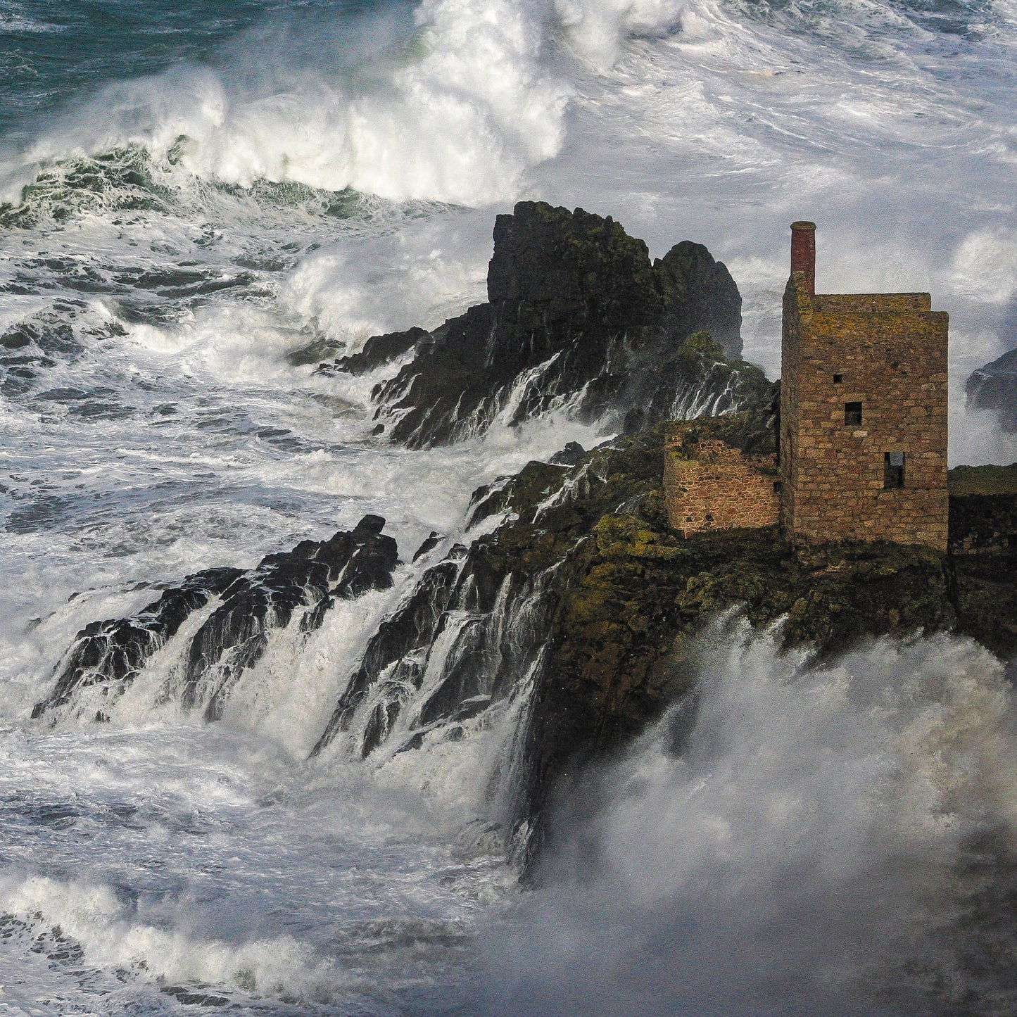An Evocative Cornwall greetings card showing a Cornish engine house perched on the rocks near Land's End with crashing, ocean waves churning around it