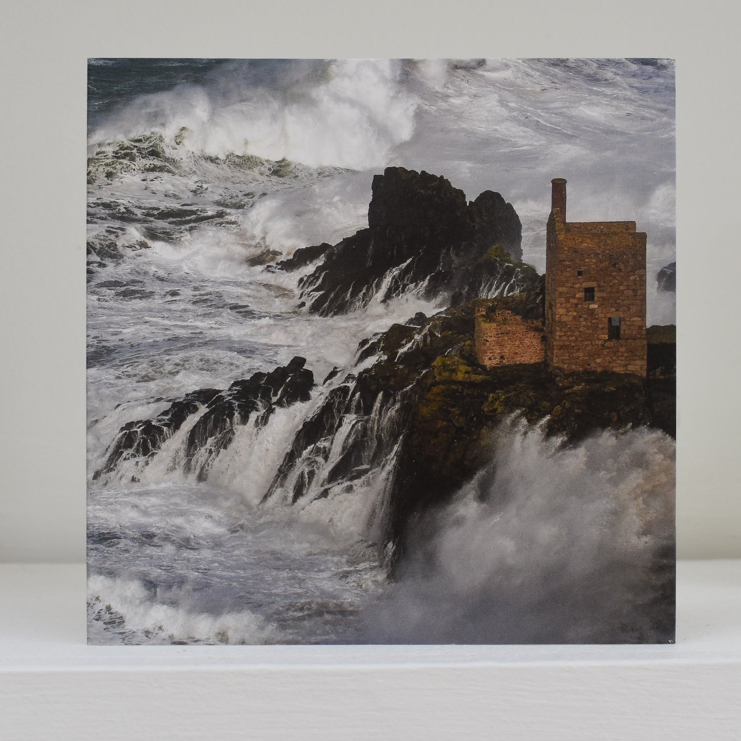 Image of card on shelf showing The Crowns at Botallack, while huge waves crash over the rocks below