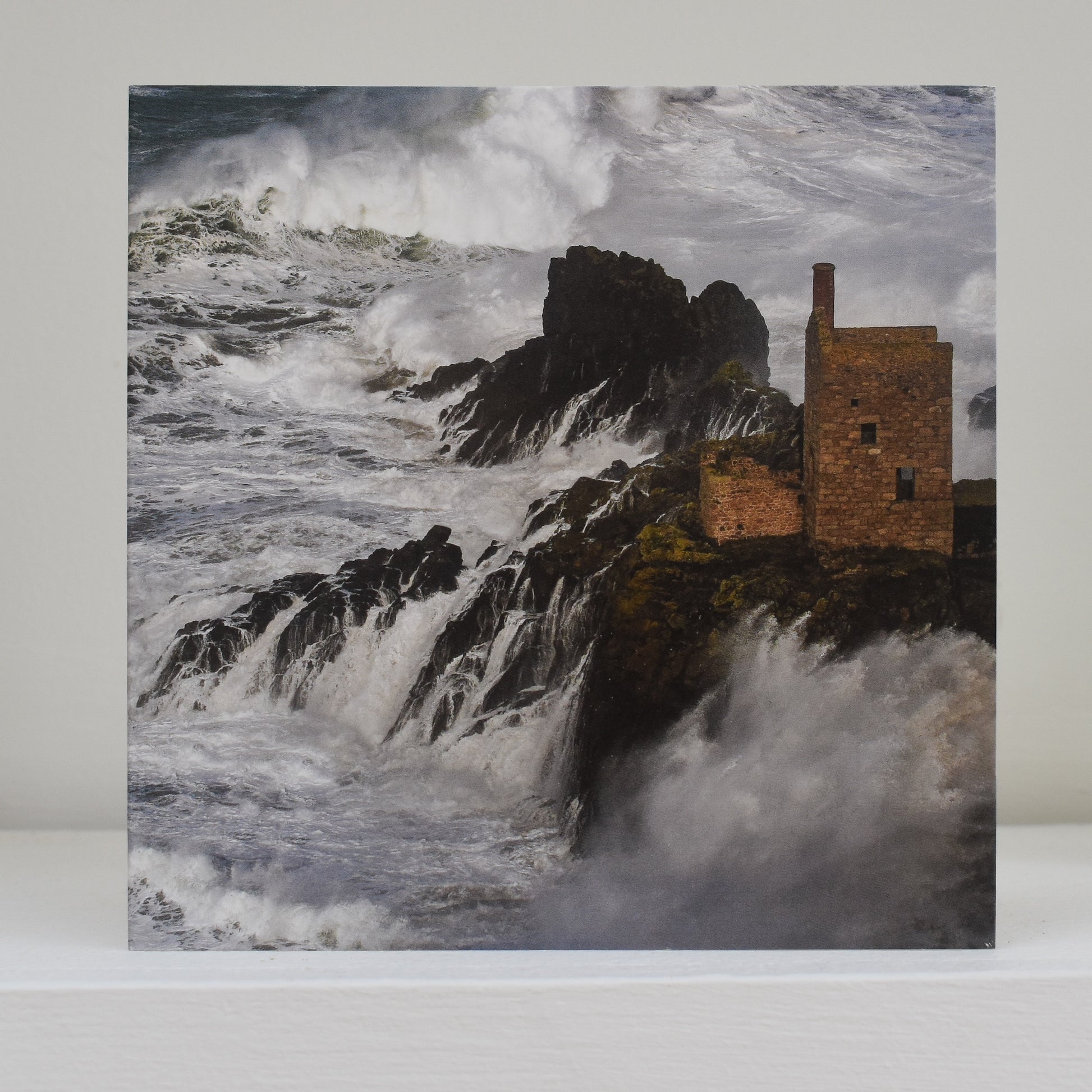 Image of card on shelf showing The Crowns at Botallack, while huge waves crash over the rocks below
