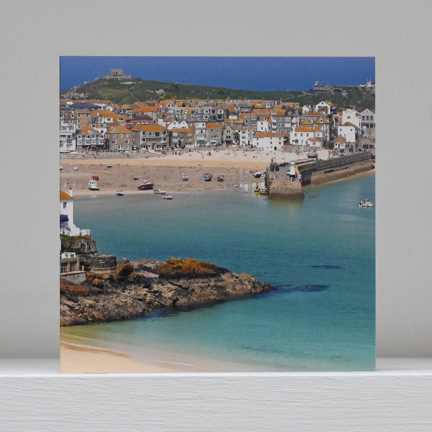 Greetings card on shelf showing image of St Ives 'island' with the iconic orange roofs, white sandy beach and turquoise water