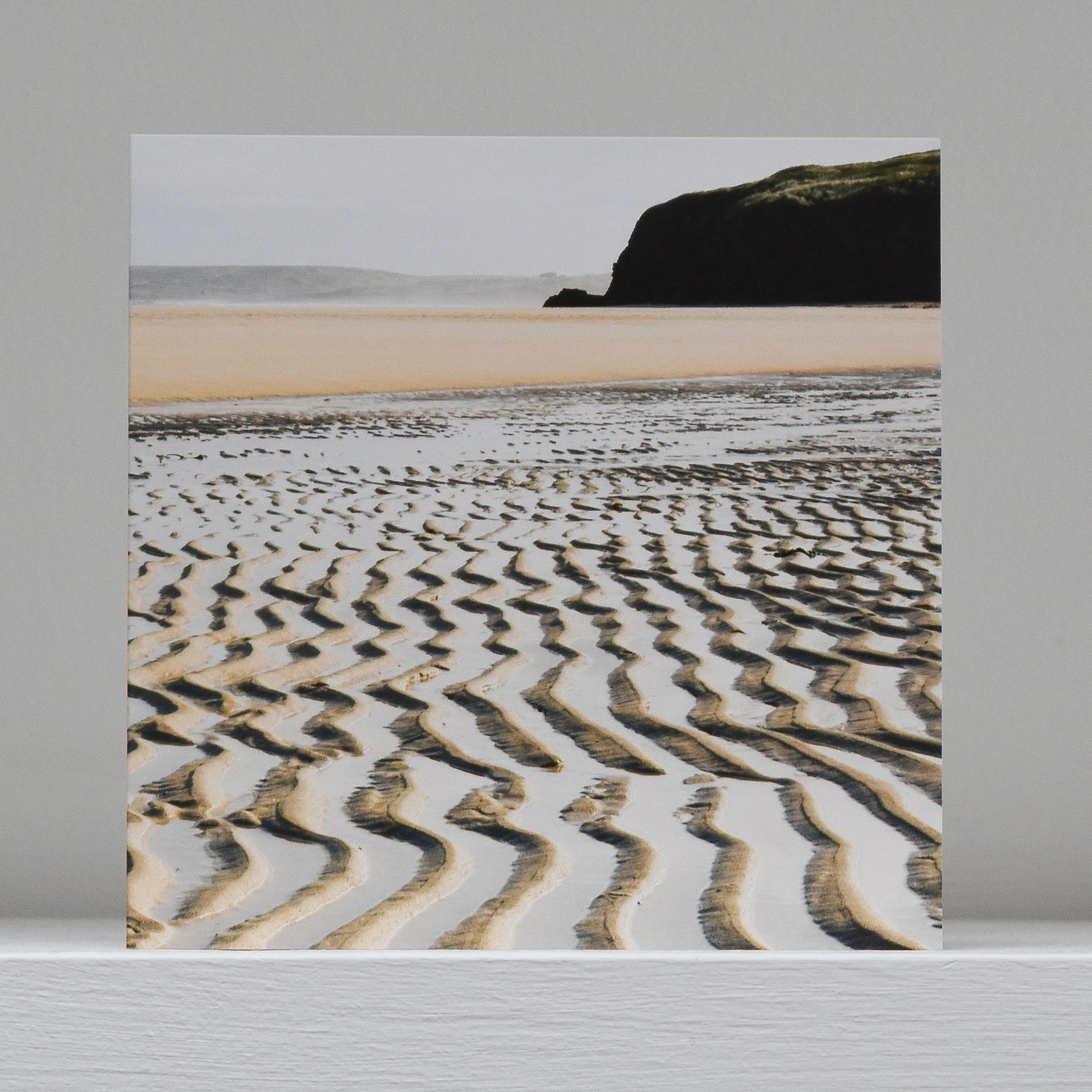 Greetings card on shelf showing image of ripples in the sand with the extent of Hayle sands and dark cliffs behind
