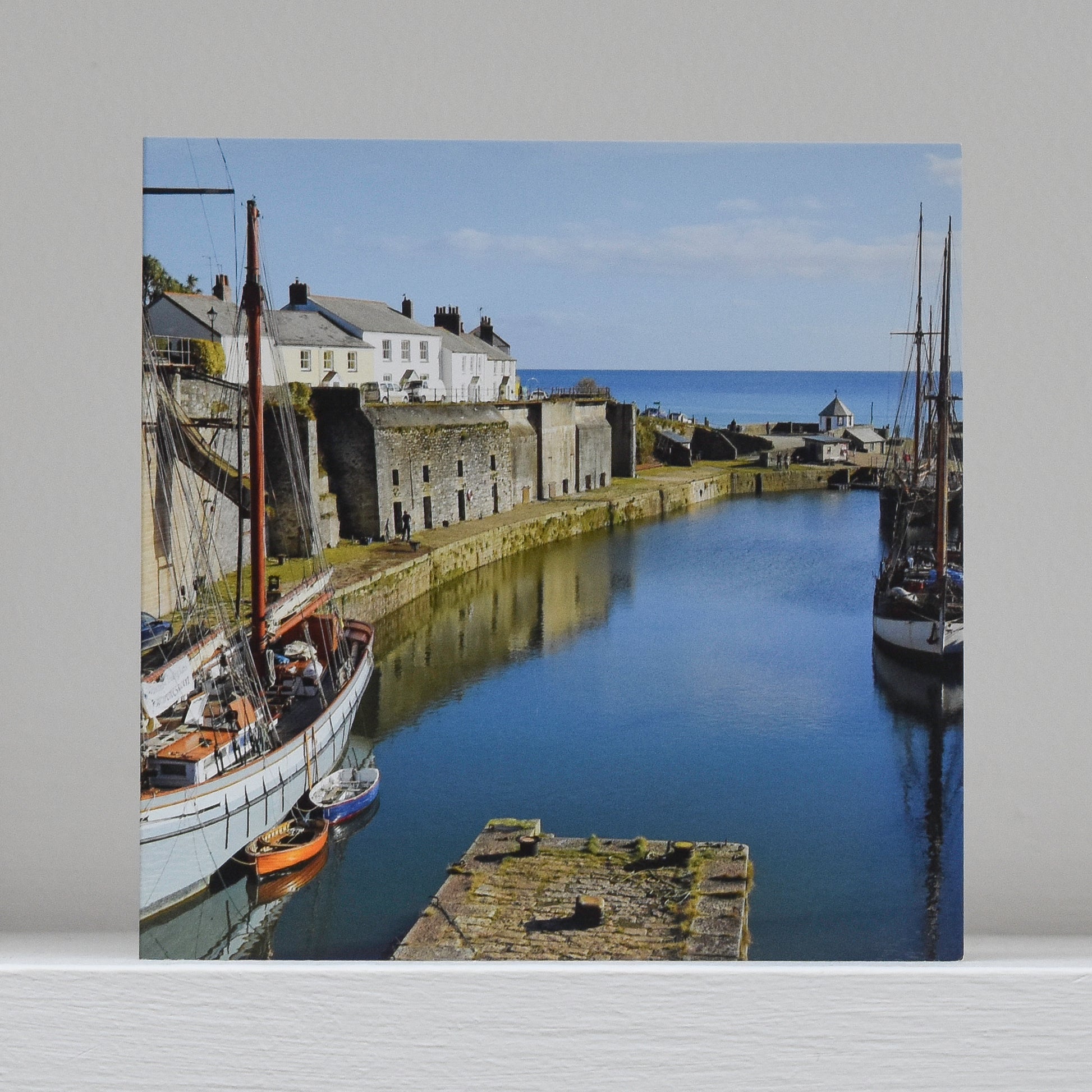 Greetings card on shelf showing image of Charlestown Harbour on a beautifully still, clear day.  Three tall ships moored up.