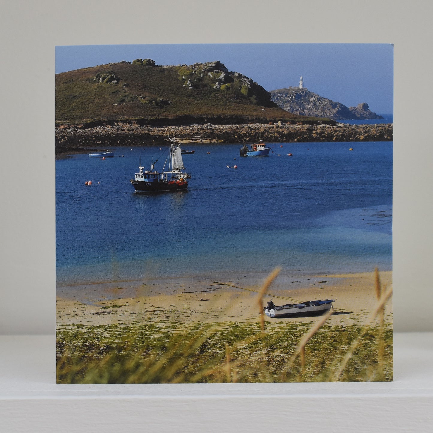 Greeting card on shelf showing image by Sarah Lay of fishing boats in the Isles of Scilly, with Round House Light in the distance