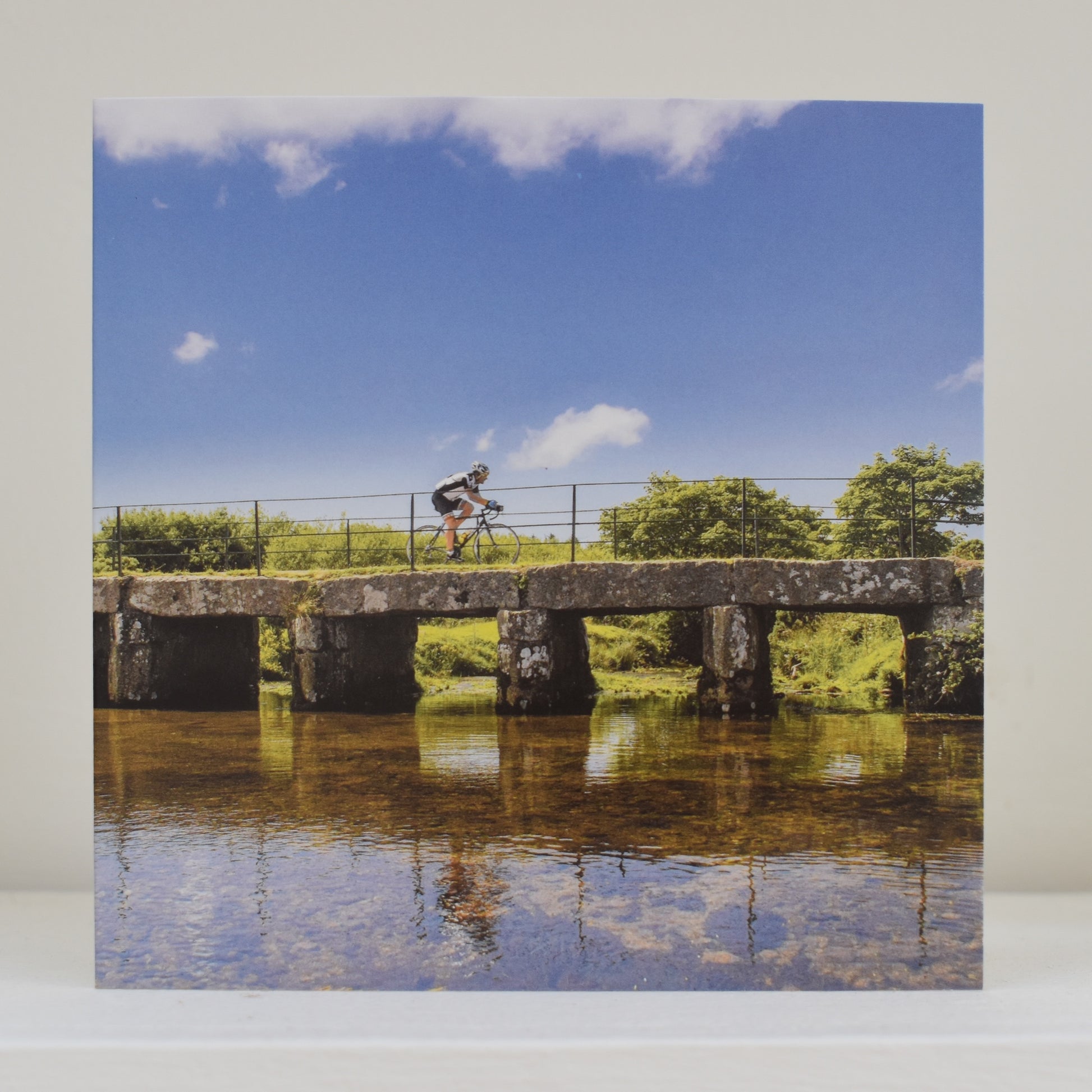 Greeting card on shelf, with an image by Janie Smith showing a cyclist crossing the clapper bridge at Delank on Bodmin Moor