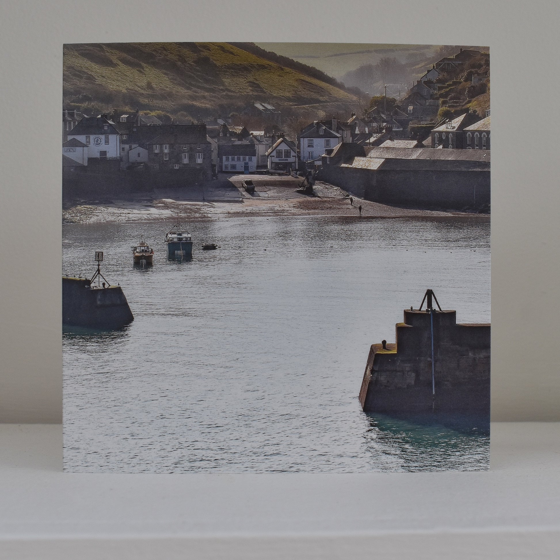 Greeting card on shelf, showing an image of Port Isaac in the first light of early morning, through the entrance to the harbour