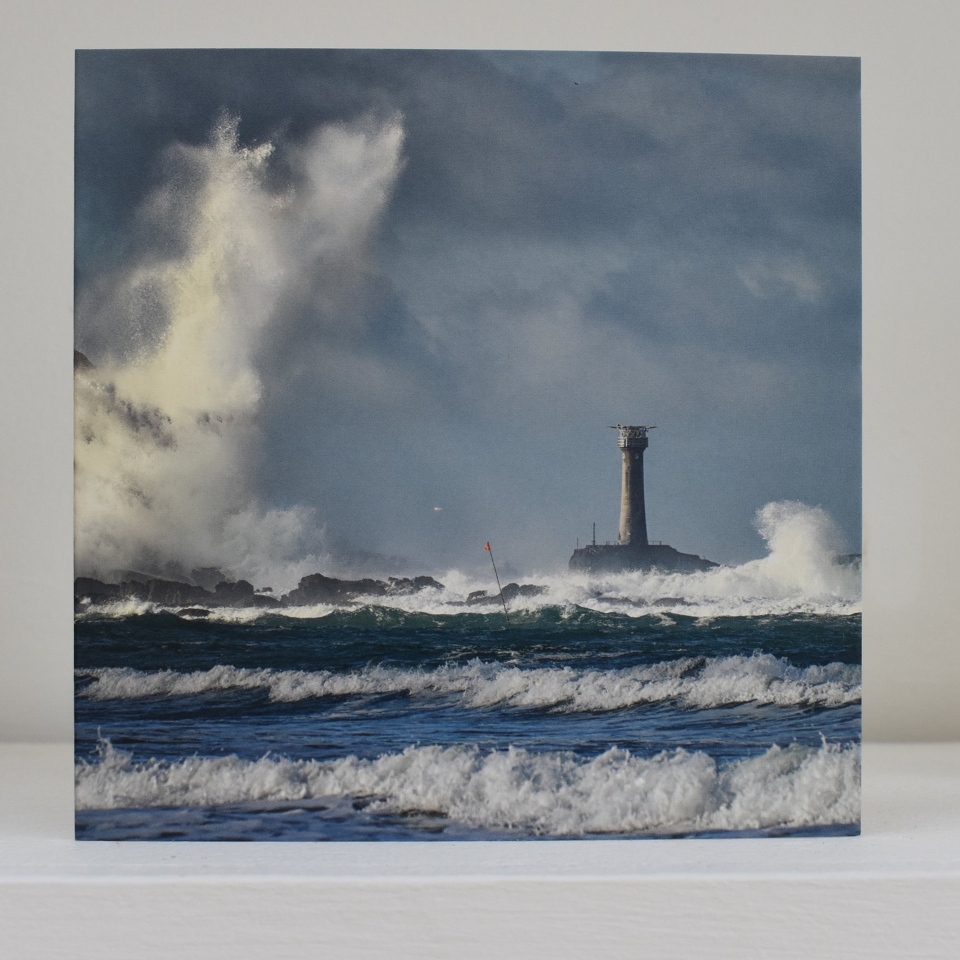 Greeting card on shelf, showing an image by Peter Maddern of Longships Lighthouse amid stormy seas