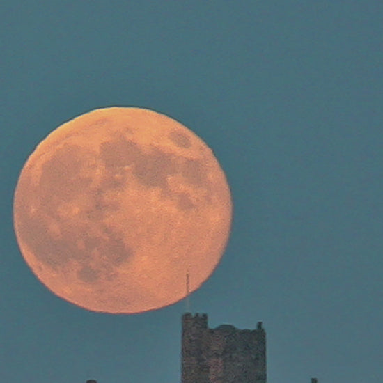 Video animation of a greetings card image, showing an orange super moon in a deep blue sky, just rising over St Michael's Mount