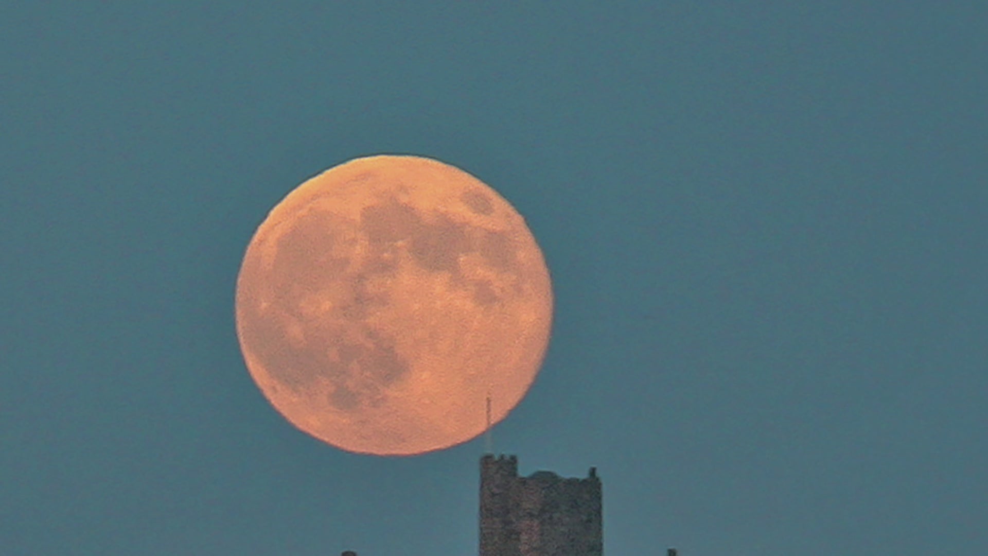 Video animation of a greetings card image, showing an orange super moon in a deep blue sky, just rising over St Michael's Mount