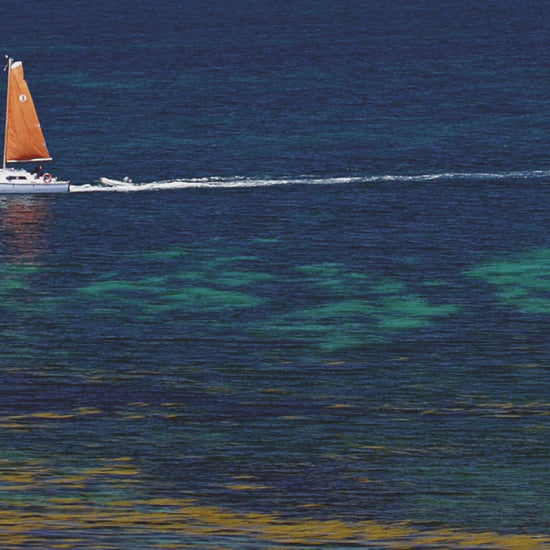 Video animatio of greeting card showing catamaran with orange sail  passing Round Island in the Isles of Scilly, with blue and azure water